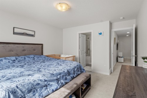 Carpeted bedroom featuring light gray walls, a built-in light fixture, and an open doorway revealing a bathroom with a shower-tub combination - 1471 Plum Circle Circle, Edmonton, AB - Indoor Photo Showing Bedroom