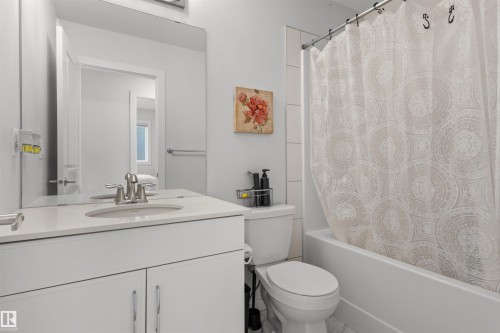 Contemporary bathroom featuring a single vanity with a white countertop and undermount sink, a large wall-mounted mirror, white shaker-style cabinetry, and a full bathtub with a shower - 1471 Plum Circle Circle, Edmonton, AB - Indoor Photo Showing Bathroom