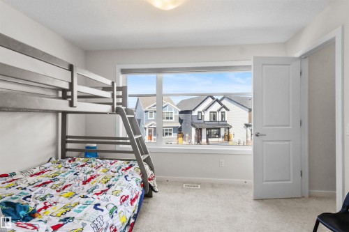 Bedroom featuring light gray carpeting, a large window with white trim, and a white interior door with a silver handle - 1471 Plum Circle Circle, Edmonton, AB - Indoor Photo Showing Bedroom