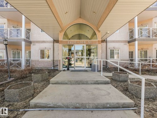 Multi-story building exterior featuring a covered entryway with an arched glass transom, full glass entry doors, and concrete steps with a white metal handrail - 317 2420 108 Street, Edmonton, AB - Outdoor With Balcony
