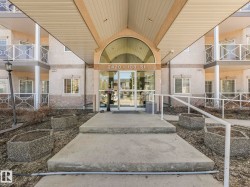 Multi-story building exterior featuring a covered entryway with an arched glass transom, full glass entry doors, and concrete steps with a white metal handrail - 