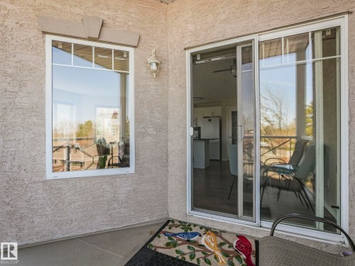 Exterior patio featuring a textured stucco finish, white frame windows with upper divided lites, and a sliding glass door with a screen - 317 2420 108 Street, Edmonton, AB - Outdoor With Exterior