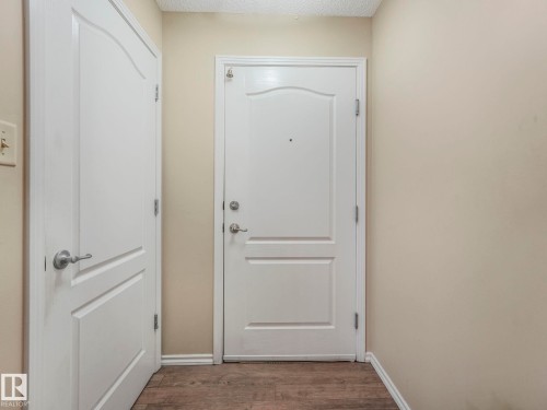 Entryway featuring a solid panel door with brushed nickel hardware, light neutral wall paint, white baseboards, and wood-finish flooring - 317 2420 108 Street, Edmonton, AB - Indoor Photo Showing Other Room