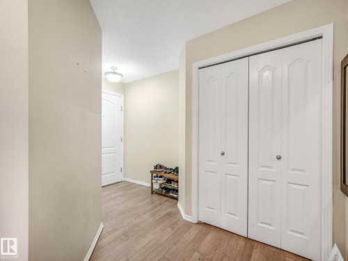 Entryway featuring wood-finish flooring, a white paneled door, and a built-in double-door closet with recessed paneling - 317 2420 108 Street, Edmonton, AB - Indoor