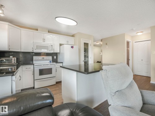 Bright kitchen featuring white cabinetry, dark countertops, a white appliance suite, and wood-finish flooring - 317 2420 108 Street, Edmonton, AB - Indoor Photo Showing Kitchen