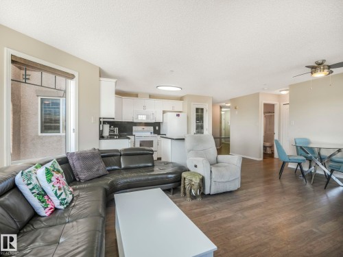 Open-concept living area featuring wood-finish flooring, a kitchen with white cabinetry and black countertops, and a dining area with a glass-top table - 317 2420 108 Street, Edmonton, AB - Indoor Photo Showing Living Room