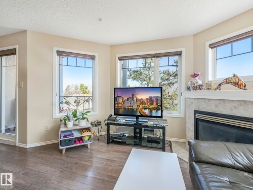 Living area featuring wood-finish flooring, a fireplace with a tiled surround and mantel, and multiple windows with blinds - 317 2420 108 Street, Edmonton, AB - Indoor Photo Showing Living Room With Fireplace