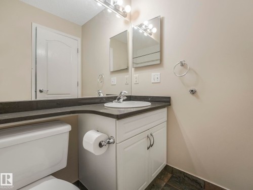 Bathroom vanity with an integrated sink, dark countertop, and white cabinetry - 317 2420 108 Street, Edmonton, AB - Indoor Photo Showing Bathroom