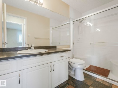 Bathroom featuring a white vanity with an undermount sink, dark countertop, and a mirrored wall - 317 2420 108 Street, Edmonton, AB - Indoor Photo Showing Bathroom