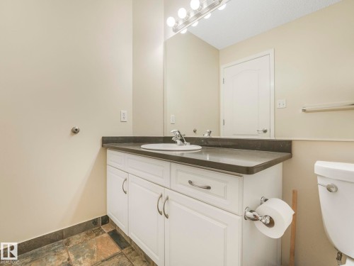 Vanity with a surface-mount sink, dark countertop, and white cabinetry featuring chrome hardware - 317 2420 108 Street, Edmonton, AB - Indoor Photo Showing Bathroom