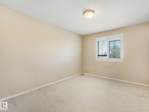 Neutral-toned bedroom featuring wall-to-wall carpeting, a multi-pane window with horizontal blinds, and a semi-flush mount ceiling light fixture - 317 2420 108 Street, Edmonton, AB - Indoor Photo Showing Other Room