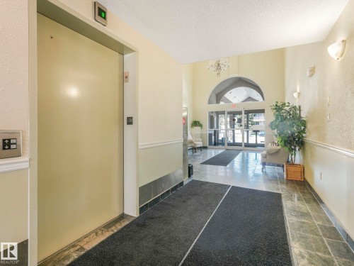 Building entryway featuring an elevator, tile flooring, wall sconces, and a glass-paneled entry door with an arched transom - 317 2420 108 Street, Edmonton, AB - Indoor Photo Showing Other Room