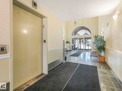 Building entryway featuring an elevator, tile flooring, wall sconces, and a glass-paneled entry door with an arched transom - 