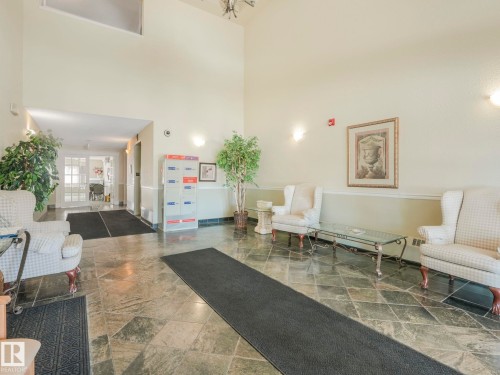 Spacious lobby featuring stone tile flooring, high ceilings, decorative wall sconces, and double glass-paneled doors - 317 2420 108 Street, Edmonton, AB - Indoor