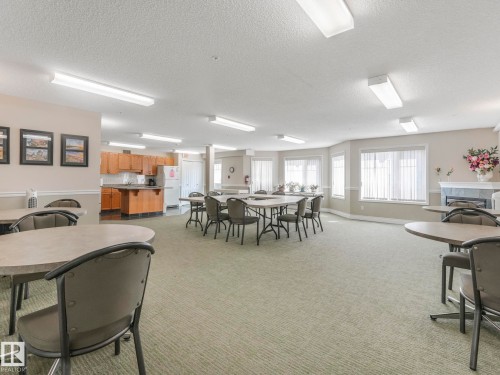 Spacious common area featuring textured carpeting, multiple window bays with blinds, and a built-in fireplace with a mantel - 317 2420 108 Street, Edmonton, AB - Indoor Photo Showing Dining Room