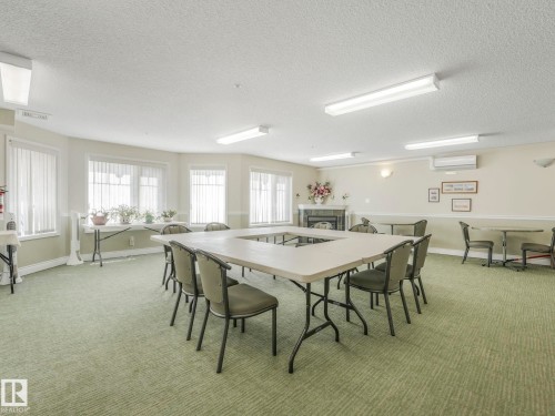 Spacious room featuring patterned green carpeting, multiple windows with vertical blinds, a decorative fireplace, and recessed lighting - 317 2420 108 Street, Edmonton, AB - Indoor Photo Showing Dining Room