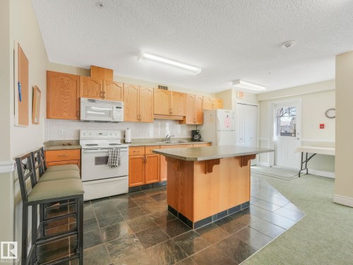 Kitchen space featuring full-height wood cabinetry, white tile backsplash, and a central island with a stone-finish countertop - 317 2420 108 Street, Edmonton, AB - Indoor Photo Showing Kitchen