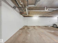 Underground parking space featuring a concrete floor, overhead piping, and fluorescent lighting - 