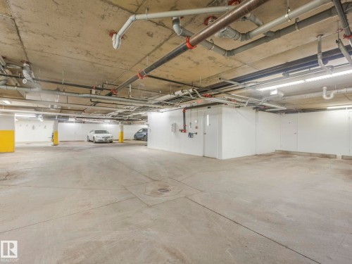 Underground parking garage featuring concrete flooring and ceiling, exposed utility piping, fluorescent strip lighting, and yellow-painted support columns - 317 2420 108 Street, Edmonton, AB - Indoor Photo Showing Garage
