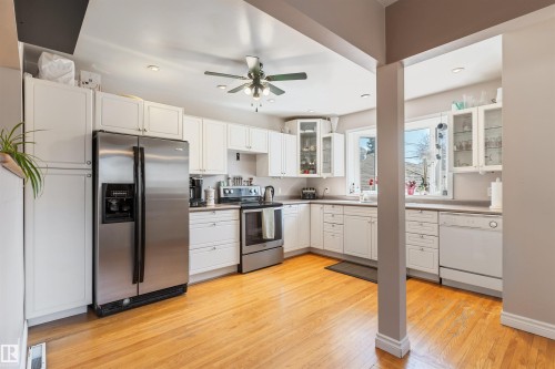 Bright kitchen featuring light wood-finish flooring, white cabinetry, and stainless steel appliances - 10803 52 Street, Edmonton, AB - Indoor Photo Showing Kitchen