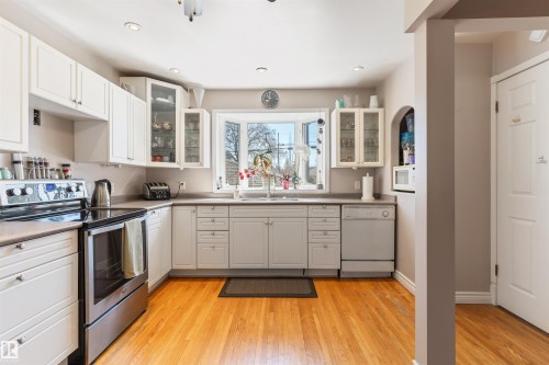 Bright kitchen featuring light wood-finish flooring, white cabinetry, stainless steel appliances, a large bay window, and recessed lighting - 10803 52 Street, Edmonton, AB - Indoor Photo Showing Kitchen