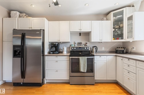 Kitchen featuring white cabinetry, stainless steel appliances, wood-finish flooring, recessed lighting, and glass-front upper cabinets - 10803 52 Street, Edmonton, AB - Indoor Photo Showing Kitchen
