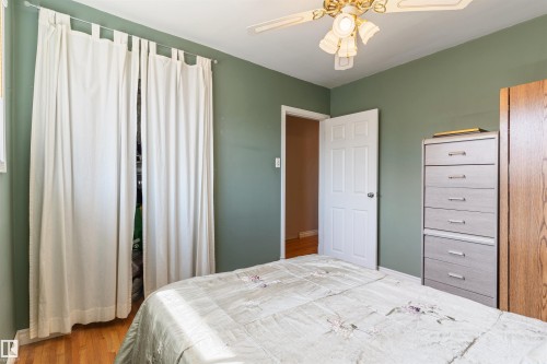 Bedroom featuring hardwood flooring, a ceiling fan with integrated lighting, and a white six-panel door - 10803 52 Street, Edmonton, AB - Indoor Photo Showing Bedroom