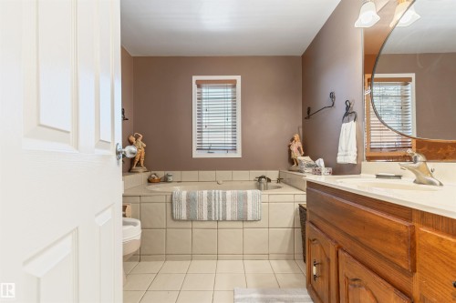 Bathroom featuring a built-in tub with tile surround, a wood vanity with integrated sink, and white window blinds - 10803 52 Street, Edmonton, AB - Indoor Photo Showing Bathroom
