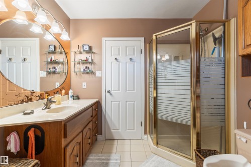 Bathroom featuring a wood-finish vanity with an integrated sink and light-toned countertop, an oval mirror, and an enclosed shower with frosted glass panels and brass-tone framing - 10803 52 Street, Edmonton, AB - Indoor Photo Showing Bathroom