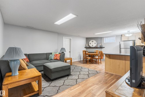 Open-concept living area featuring light wood-finish flooring, recessed lighting, and a gray brick accent wall with a fireplace - 10803 52 Street, Edmonton, AB - Indoor