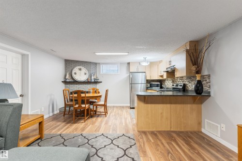 Open-concept living space featuring wood-finish flooring, a kitchen with light wood cabinetry and dark countertops, stainless steel appliances, and a tiled backsplash - 10803 52 Street, Edmonton, AB - Indoor