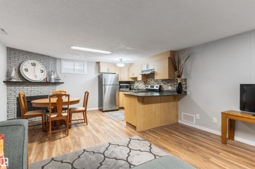 Open-concept living area featuring wood-finish flooring, a kitchen with light wood cabinetry and stainless steel appliances, a grey brick-faced fireplace, and a dining area with a round table - 10803 52 Street, Edmonton, AB - Indoor