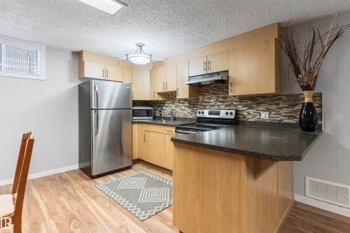 Full kitchen featuring wood-finish cabinetry, stainless steel refrigerator, black electric range, and a mosaic tile backsplash - 10803 52 Street, Edmonton, AB - Indoor Photo Showing Kitchen With Double Sink