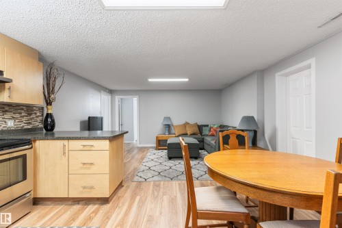 Open-concept kitchen and living area featuring wood-finish flooring, light wood cabinetry, a tiled backsplash, and a built-in stainless steel range - 10803 52 Street, Edmonton, AB - Indoor