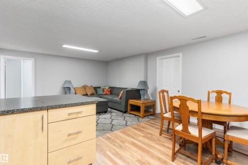 Open-concept living space with light-toned wood-finish flooring, a kitchen island featuring a dark countertop and light wood cabinetry, and recessed lighting fixtures - 10803 52 Street, Edmonton, AB - Indoor