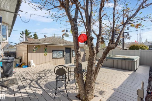 Expansive wood-finish deck featuring a built-in hot tub, a detached garage with vertical siding, and a privacy fence - 10803 52 Street, Edmonton, AB - Outdoor With Deck Patio Veranda