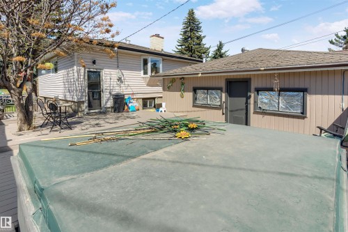 Exterior deck space featuring a covered hot tub, mature trees, and a detached structure with a pitched roof - 10803 52 Street, Edmonton, AB - Outdoor