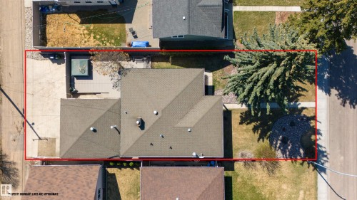 Aerial view showcasing the property's layout, featuring a sloped roofline, an expansive concrete driveway, a rear deck, and established trees - 10803 52 Street, Edmonton, AB - 