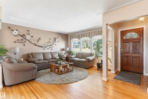 Warm and inviting living area featuring wood-finish flooring, a large picture window, and a paneled entry door with an arched glass insert - 10803 52 Street, Edmonton, AB - Indoor Photo Showing Living Room