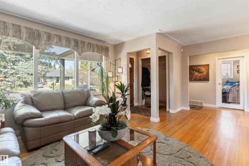 Living room featuring wood-finish flooring, a large bay window, crown molding, and an attached lighting fixture - 10803 52 Street, Edmonton, AB - Indoor Photo Showing Living Room