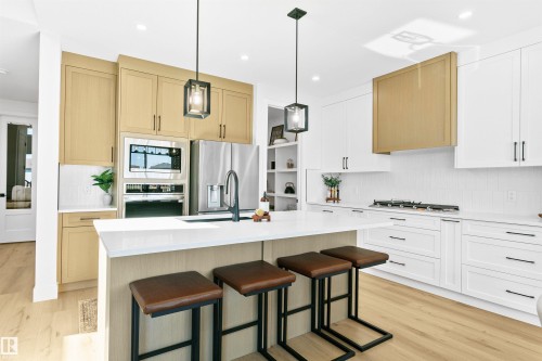 Spacious kitchen featuring an extended island with seating, a gas range, built-in stainless steel appliances, a white subway tile backsplash, and wood-finish flooring - 34 Harley Way, Spruce Grove, AB - Indoor Photo Showing Kitchen With Upgraded Kitchen