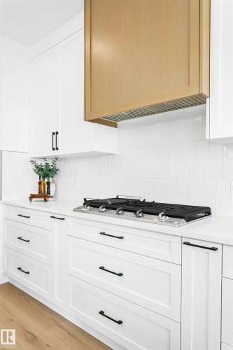 Modern kitchen featuring a light wood-finish range hood, white shaker cabinetry with matte black hardware, a built-in gas cooktop, and a white tile backsplash - 34 Harley Way, Spruce Grove, AB - Indoor Photo Showing Kitchen