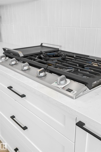 Stainless steel gas range with griddle attachment, white shaker-style cabinetry, matte black hardware, and a white subway tile backsplash - 34 Harley Way, Spruce Grove, AB - Indoor