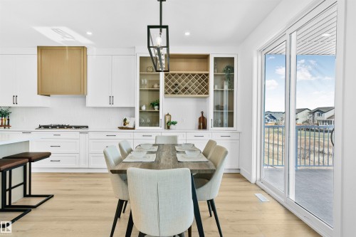 Open-concept kitchen and dining area featuring light wood-finish flooring, white cabinetry, a built-in wine rack, and a gold-tone range hood - 34 Harley Way, Spruce Grove, AB - Indoor Photo Showing Dining Room