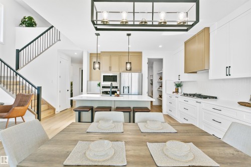 Open-concept kitchen and dining area featuring light wood-finish flooring, white cabinetry with dark hardware, a center island with pendant lighting, stainless steel appliances, and a gas cooktop - 34 Harley Way, Spruce Grove, AB - Indoor