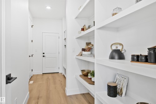 Custom built-in shelving with ample storage, complemented by wood-finish flooring and modern white doors with matte black hardware - 34 Harley Way, Spruce Grove, AB - Indoor Photo Showing Other Room