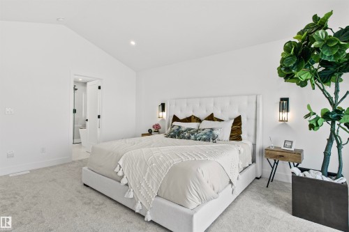 Bedroom featuring vaulted ceilings, light-toned carpeting, a white upholstered headboard, wall-mounted sconces, and an en-suite bathroom with a glass shower enclosure - 34 Harley Way, Spruce Grove, AB - Indoor Photo Showing Bedroom