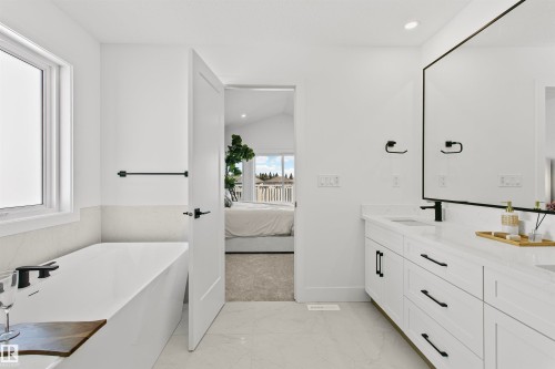 Modern bathroom featuring a freestanding tub, a dual vanity with quartz countertops, a large rectangular mirror, and matte black fixtures - 34 Harley Way, Spruce Grove, AB - Indoor