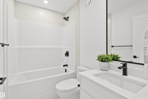 Bathroom featuring a white bathtub/shower combination with black fixtures, a white vanity with an integrated sink, a white countertop, and a large wall-mounted mirror - 34 Harley Way, Spruce Grove, AB - Indoor Photo Showing Bathroom