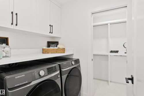 Laundry area featuring white cabinetry with black hardware, a light-toned countertop, and a built-in closet with shelving - 34 Harley Way, Spruce Grove, AB - Indoor Photo Showing Laundry Room